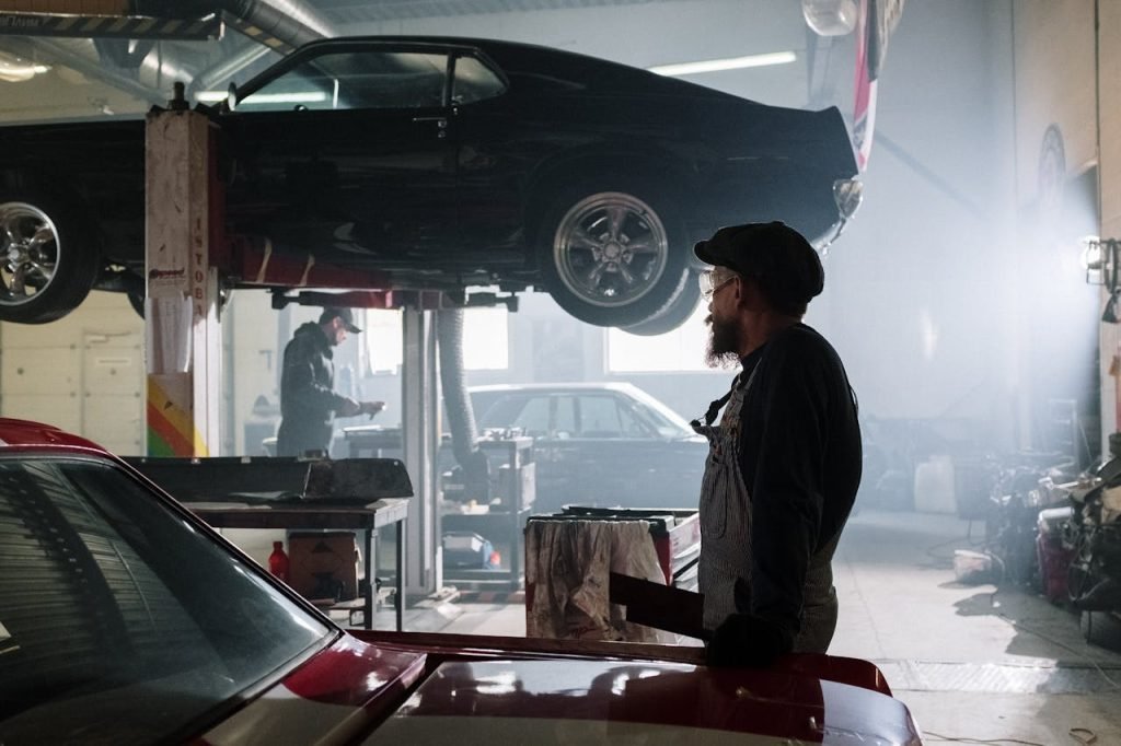Mechanics busy at work in a dimly lit auto repair garage with a raised car.